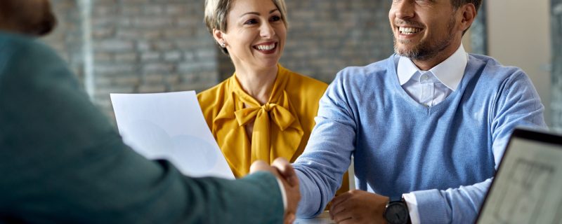 Happy couple shaking hands with real estate agent after successful agreement in the office.